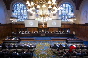 Inside image of the International Court of Justice with the justices sitting at a long table in front of windows.
